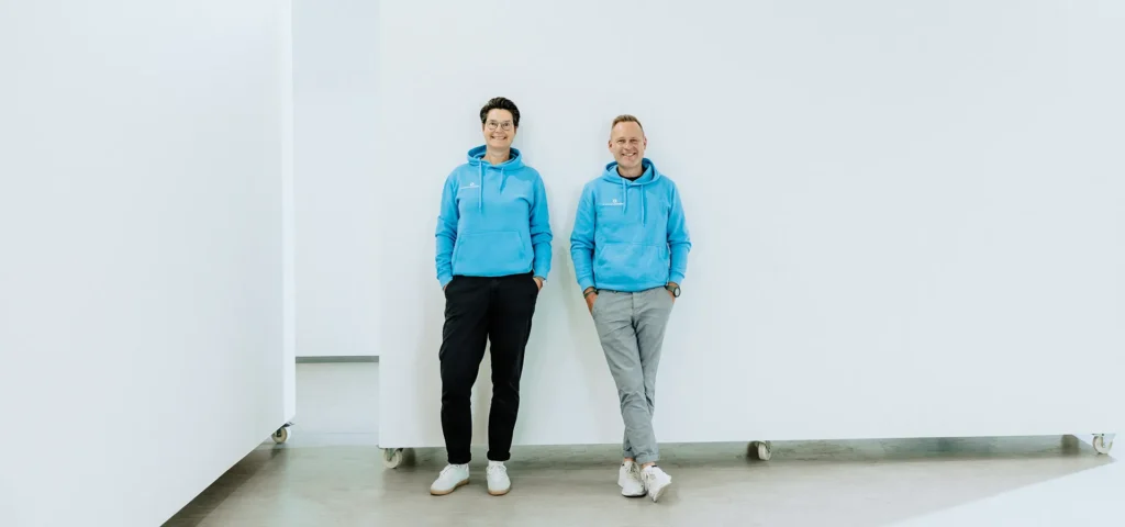 Die Coaches Stefanie Schmaus und Steffen Karpstein stehen an einer weißen Wand
